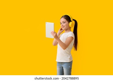 Little girl with tablet computer listening to audiobook on color background - Powered by Shutterstock