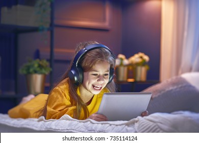 Little girl with tablet and headphones on the bed at home. Child girl listening to music.  - Powered by Shutterstock