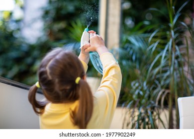 A little girl takes care of balcony flowers, refreshing them from a spray bottle. - Powered by Shutterstock