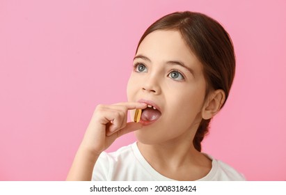 Little Girl Taking Fish Oil Pill On Color Background