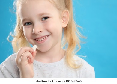 Little Girl Taking Vitamin Pill On Light Blue Background, Closeup
