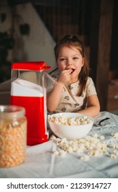 A Little Girl Tastes Ready-made Popcorn Cooked In A Popcorn Machine At Home. It's Delicios And She Smiles