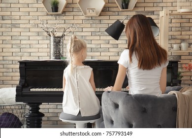 Little girl with teacher learning to play piano indoors