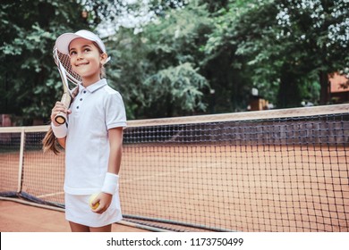 Little Girl With Tennis Racket And Ball In Sport Club. Active Exercise For Kids. Summer Activities For Children. Training For Young Kid. Child Learning To Play.