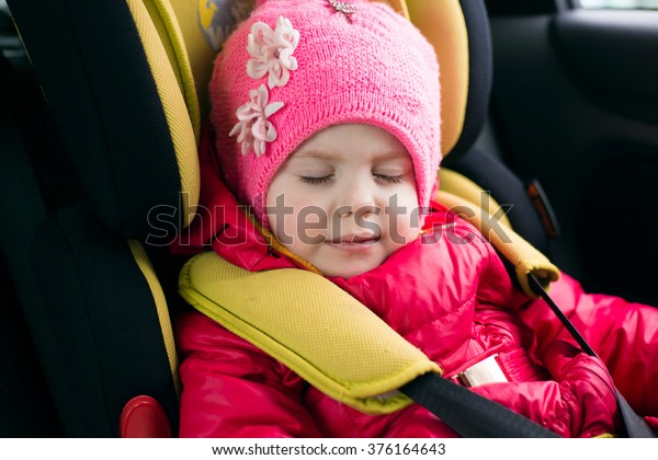 little girl three years traveling in the winter in a\
red jacket and a pink hat sleeping in a car in the child car seat\
fastened and is safe