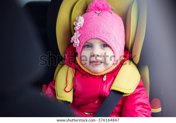 a\
little girl of three years in winter in a red jacket and a pink hat\
sitting in a car in a child car seat is going on a journey, and\
strapped is secure, smiling and builds funny\
faces