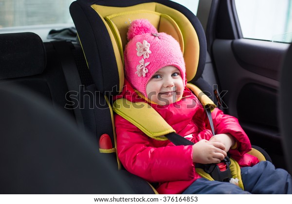 a\
little girl of three years in winter in a red jacket and a pink hat\
sitting in a car in a child car seat is going on a journey, and\
strapped is secure, smiling and builds funny\
faces
