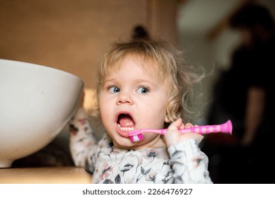 little girl toddler brushing her teeth with a pink toothbrush in the bathroom by the sink to avoid tooth decay - Shutterstock ID 2266476927