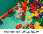 Little girl, toddler with builds a tower with a large multi-colored construction set. Play area for children. Large multi-colored construction set for children in the playroom. Montessori toys.