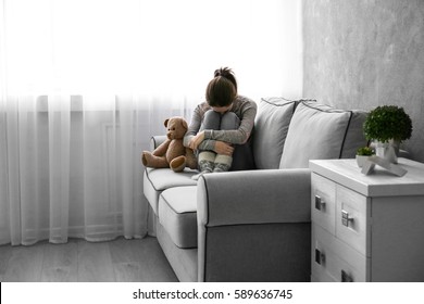 Little girl with toy bear on sofa in room