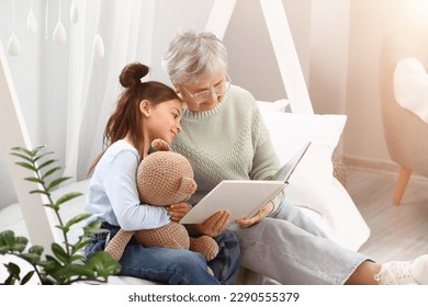 Little girl with toy and her grandmother reading book in bedroom - Powered by Shutterstock