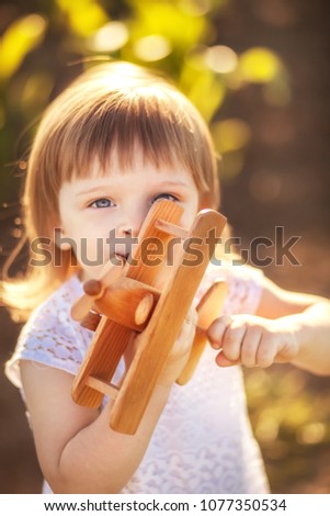 Little girl with toy wooden airplane in summer field