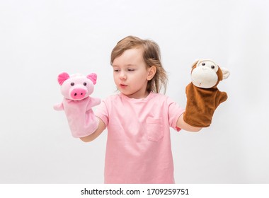 A little girl with toys on her hands on a white background with an open seat. Cute Girl playing with toys in the hands of a Puppet theater.
