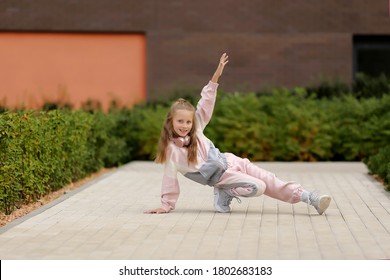 Little Girl In A Tracksuit Is Dancing Modern Dance On The Street. Young Urban Hip Hop Dancer