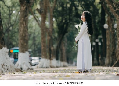 little girl in traditional costume Vietnam stood on the road with beautiful trees at sunset in Hanoi, Vietnam.