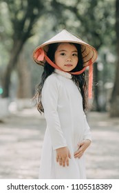 little girl in traditional costume Vietnam stood on the road with beautiful trees at sunset in Hanoi, Vietnam