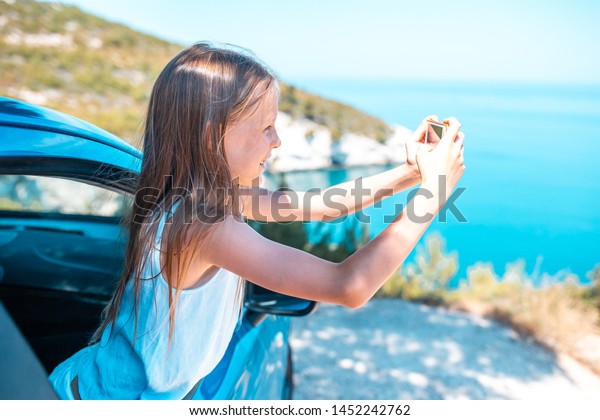 Little girl traveling by\
car and making photo of beautiful nature. Summer holiday and car\
travel concept