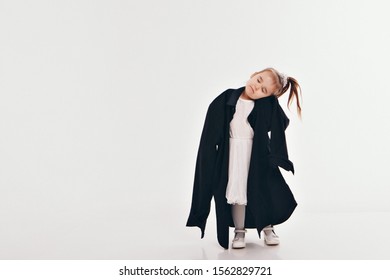 A Little Girl Tries On Dad's Shirt. Child In Big Black Clothes On White Background. Concept Of Children's Games, Imitation Of Adult Life, Fashion