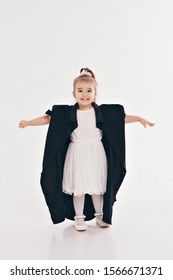 A Little Girl Tries On Dad's Shirt. Child In Big Black Clothes On White Background. Concept Of Children's Games, Imitation Of Adult Life, Fashion