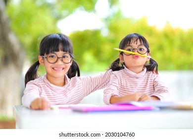 Little Girl Two Asian Wearing Glasses And Doing Homework Together At Home  Which Increases The Development And Enhances Outside The Classroom Learning Skills Concept.