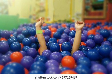 The Little Girl Is Under A Plastic Ball In Ball Pit. She Lifted Her Arms And Made Fun Sounds.            