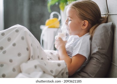 Little girl use inhaler nebulizer lying in bed in bedroom. Child asthma inhaler, nebulizer steam, flu or cold concept. Copyspace