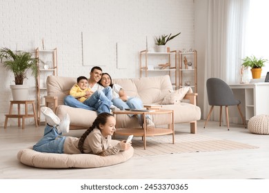 Little girl using mobile phone while her family watching TV at home - Powered by Shutterstock