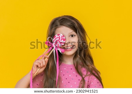 A little girl with very beautiful hair and a pink dress is holding a lollipop in her hands, A very joyful and cheerful girl with a big candy on a stick on an isolated background. Foto d'archivio © 