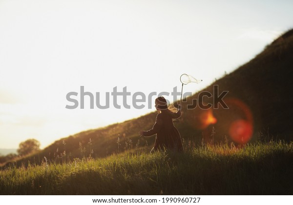Little girl\
is walking with butterfly net and catching butterflies on the green\
hills on sunny summer day. copy\
space.