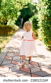 Little girl walks along the paving stones in a park. Back view - Shutterstock ID 2180121269