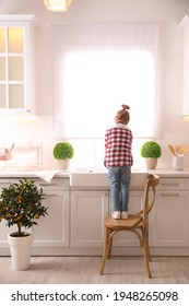 Little Girl Washing Dishes In Kitchen At Home, Back View