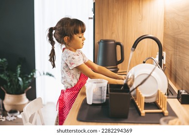 Little girl washing dishes with sponge in kitchen sink at home. Child doing chores concept.