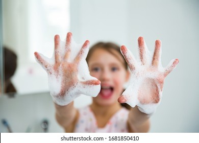 Little girl washing hands with water and soap in bathroom. Happy kid showing soapy palms. Hands hygiene and virus infections prevention. 