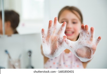 Kleines Mädchen wäscht die Hände mit Wasser und Seife im Badezimmer. Glückliches Kind, das Seifenpalmen zeigt. Hände Hygiene und Virusinfektionen Prävention. 