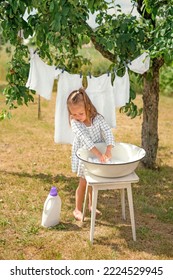 A little girl is washing  linen in the garden under a tree and hanging snow-white pure clothes to dry in the fresh air. Eco-friendly detergent for laundry - Shutterstock ID 2224529945