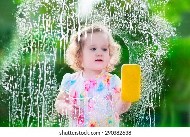 Little Girl Washing A Window. Kids Clean The House. Children Help At Home. Toddler Kid Cleaning Windows And Doors Standing On A Ladder. Child Helping With Housework Holding Sponge And Soap Bottle. 