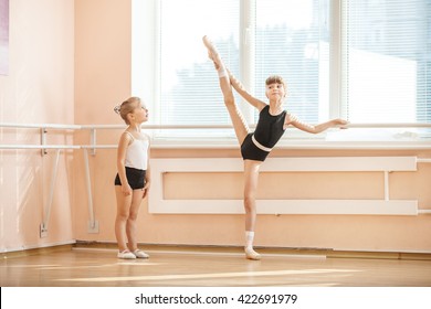 Little Girl Watching Older Ballet Student Practicing At Barre