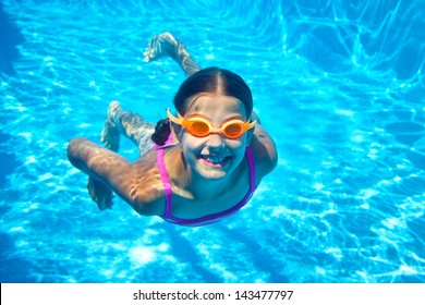 The Little Girl In The Water Park Swimming Underwater And Smiling