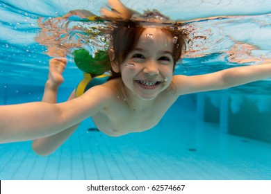 The Little Girl In The Water Park Swimming Underwater And Smiling