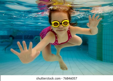 The Little Girl In The Water Park Swimming Underwater And Smiling