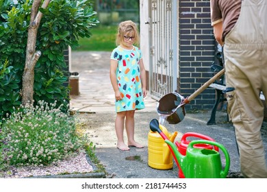 Little Girl Watering Flowers In The Garden. Child Waiting For Father Filling Water In Cans. Save Water, Drought,heat Concept. Environment In Europe Or World. Rain Water