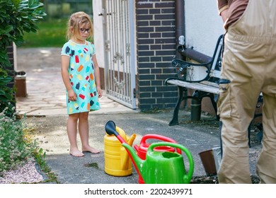 Little Girl Watering Flowers In The Garden. Child Waiting For Father Filling Water In Cans. Save Water, Drought,heat Concept. Environment In Europe Or World. Rain Water