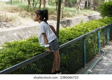 Little girl wearing black and white color cloth.Climbing on iron mash with stylish action.Green leaf around child.