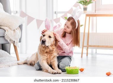 Little girl wearing bunny ears to golden retriever dog at Easter day in sunny room