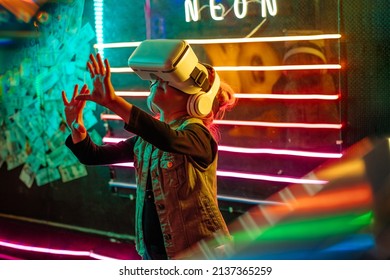 Little girl wearing glasses of virtual reality playing or watching 3d educational video on the colorful neon lights background. Generation Alpha using future technology. VR, augmented reality concept.