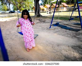 Little girl wearing the Malaysian traditional costume, Baju Kurung is playing swing in the park. Selective focus.