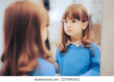 
Little Girl Wearing New Eyeglasses Looking in the Mirror. Adorable fashionable toddler wearing stylish frames in optical store
