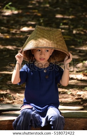 little girl wearing thai traditional dress, sitting on the floor with a bamboo basket on the head cover.