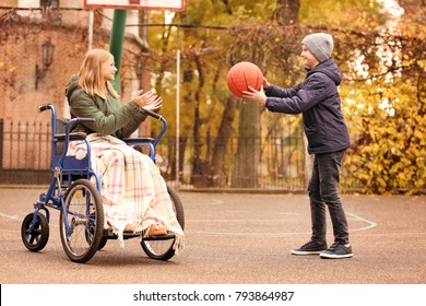 Little girl in wheelchair and boy playing with ball outdoors
