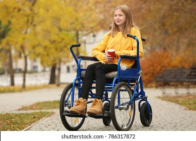 Little girl in wheelchair with cup of coffee outdoors